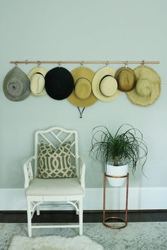 hats are hanging on the wall above a chair and potted plant in a room