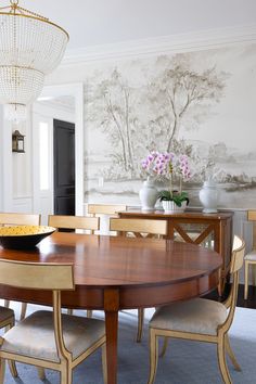 a dining room table and chairs in front of a wall with a painting on it