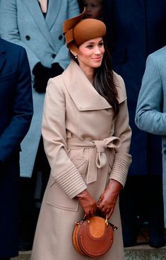 a woman in a trench coat and hat is holding a handbag while standing next to other people