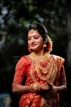 a woman in an orange and gold sari with her hands clasped together, smiling at the camera