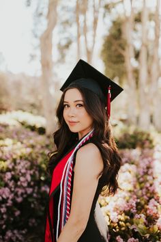 a woman wearing a graduation cap and gown standing in front of purple flowers with her hand on her hip