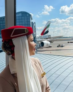 a woman wearing a red and white hat looks out the window at an airplane on the tarmac