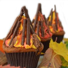 three cupcakes with chocolate frosting and candy sticks on them sitting next to leaves