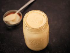 a glass jar filled with mayonnaise next to a spoon on a black surface