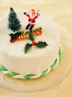 a white cake decorated with christmas decorations and santa clause on top is sitting on a glass platter