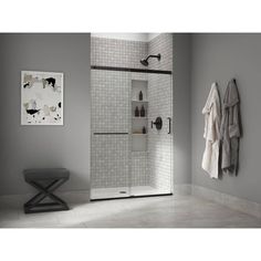 a walk in shower sitting next to a white tiled wall and grey walls with towels hanging on the rack