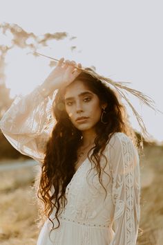 a woman with long hair wearing a white dress and holding her hat over her head