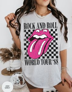 Rock on with our Kiss of Vintage Rock Tee: Tour '88! This edgy t-shirt features a bold pink kiss mouth design on the front, adding a touch of rock and roll flair to your wardrobe. With its vintage vibe and cool "Tour '88" print, this tee is perfect for music lovers and trendsetters alike. Made from high-quality cotton for maximum comfort and durability, it's the ultimate statement piece for any rock-inspired outfit. Get ready to turn heads and rock out in style with this must-have tee! *Unisex Sizing* Retro Slogan Top For Concerts, Letter Print Rock And Roll Tops For Concert, Retro Slogan Tops For Concerts, Rock And Roll Graphic Print Tops For Spring, Rock Style Text Print Top For Concert, Rock Style Tops With Text Print For Concert, Rock Style Text Print Top For Summer, Summer Rock Style Tops With Text Print, Rock Style Graphic Tops For Concert