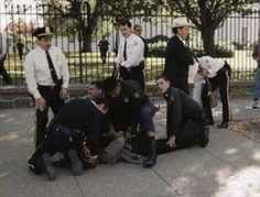 a group of police officers standing around a man laying on the ground in front of a fence