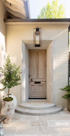 a white house with a wooden door and steps leading to the front entrance, surrounded by potted plants