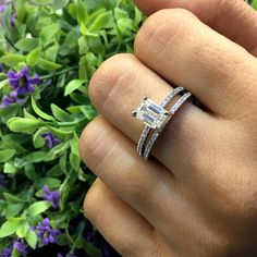 a woman's hand holding an engagement and wedding ring in front of purple flowers