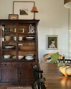 a wooden dining room table with plates and bowls on it, next to an old china cabinet