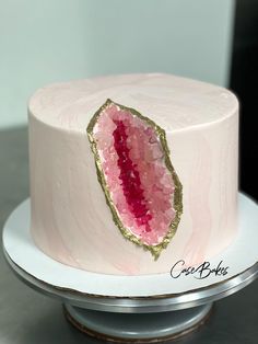 a white cake with pink and gold frosting on a silver platter next to a knife