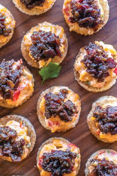 small crackers with various toppings are arranged on a wooden surface, ready to be eaten