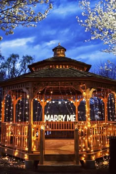 a gazebo covered in fairy lights with the words marry me on it's side