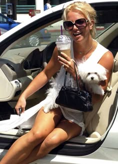 a woman sitting in the driver's seat of a car holding a small dog