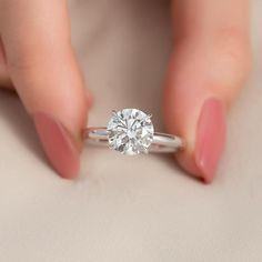 a woman's hand holding a diamond ring on top of her finger and the other hand