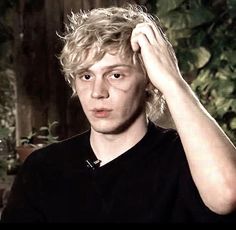 a young man with blonde hair is looking at the camera and holding his hand on his head