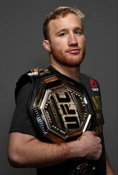 a man in a black shirt is holding a wrestling belt and looking at the camera