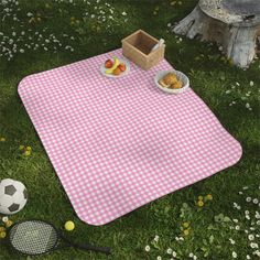 a picnic blanket on the grass with food and tennis rackets in front of it