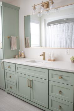 a bathroom with green cabinets and white counter tops, along with a gold faucet