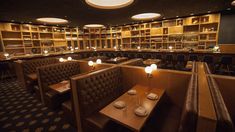 a dimly lit restaurant with wooden tables and chairs in front of the bookshelves