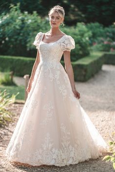 a woman in a wedding dress standing on a path with trees and bushes behind her