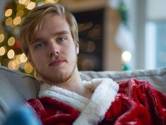 a man wrapped in a blanket sitting on top of a couch next to a christmas tree