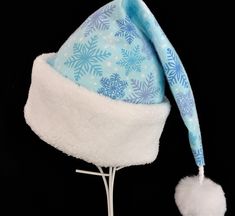 "NEW  This festive Santa hat is made up in a cozy blue and lavender snowflake patterned flannel cotton fabric. The hat is trimmed with a snowy white soft Sherpa faux fur turn up brim. Proportions of the hat are generous and will fit most head sizes, ladies or gents.    The styling is a slouch cone, traditional Santa stocking cap. Measurement for opening for your head is 24-25\" circumference and the length is 19\".  There is a snowy white faux fur pompom dangle. If you need more than the number Adjustable Blue Winter Mini Hat, Adjustable Blue Mini Hat For Winter, Adjustable Blue Mini Winter Hats, Adjustable Light Blue Winter Hat, Blue Winter Mini Hat With Curved Brim, Blue Mini Hats With Curved Brim For Winter, Blue Curved Brim Mini Hat For Winter, Blue Winter Costume Hat, Whimsical Blue Winter Hat