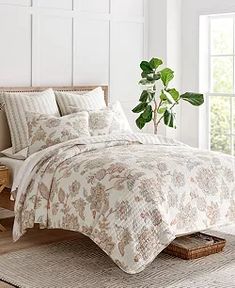 a bed with white sheets and pillows in a room next to a potted plant