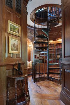 a spiral staircase in the middle of a room with bookshelves and pictures on the wall