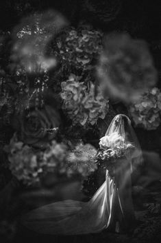 a woman in a wedding dress and veil is standing next to flowers with her face obscured by the veil