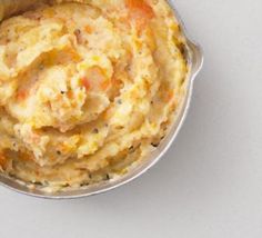 a metal bowl filled with mashed potatoes on top of a white countertop next to a wooden spoon