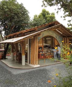 two people are standing in front of a small building with wood shinning on the roof