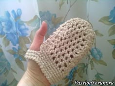 a hand holding a crocheted mitt in front of a flowered curtain