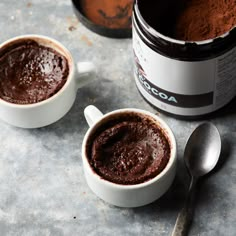 two mugs filled with chocolate pudding on top of a table next to a spoon