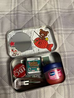 an open tin with various items in it sitting on a bed next to a mirror