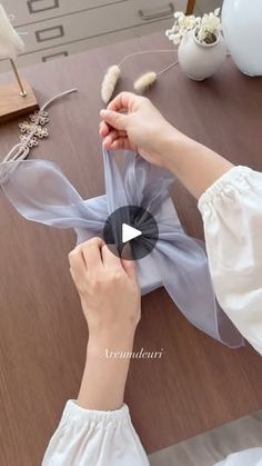 a woman is making something with sheer fabric on the table and holding it in her hands