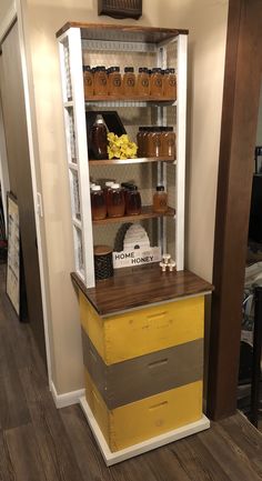 a yellow and gray cabinet with honey jars on it's shelves in a room