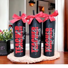 three personalized black wine bottles with red bows on the top and bottom, sitting on a table