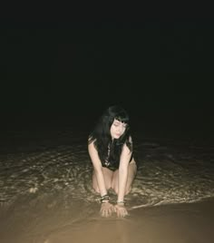 a woman sitting on the beach at night with her legs in the water and one hand under her head