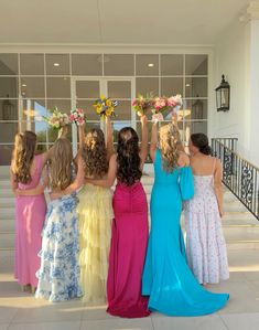 four girls in dresses are standing on the steps with their arms up and one girl is holding flowers