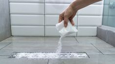 a person is pouring water into a drain in the bathroom with white tiles on the floor