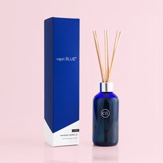 an empty blue bottle next to a box and reed diffuser on a pink background