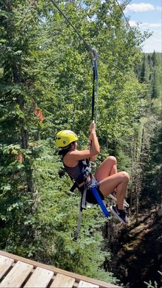 a woman is zipping through the air on a rope course in the forest with trees