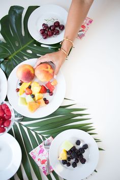 two people reaching for fruit on plates with palm leaves and flowers in the foreground