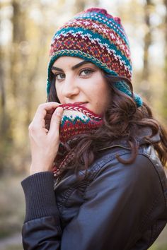 a woman wearing a knitted hat and scarf in front of a wooded area with trees