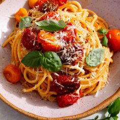 a white bowl filled with pasta, tomatoes and basil garnished with parmesan cheese