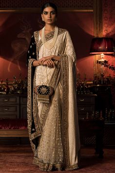 a woman wearing a white and black sari with gold detailing on the border, standing in