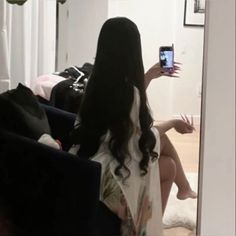 a woman taking a selfie in front of a mirror with her cell phone while sitting on a couch